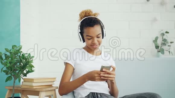 漂亮的女学生正在给朋友发短信在网上聊天在沙发上用耳机听音乐视频的预览图