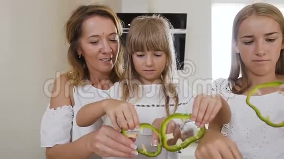 妈妈教两个孩子女儿在厨房的餐桌上做饭在家里的厨房里用生绿的辣椒母亲视频的预览图