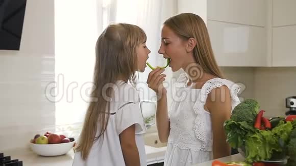 两个穿着白色连衣裙的长头发的姐妹一起在厨房里吃了一片切碎的青椒视频的预览图