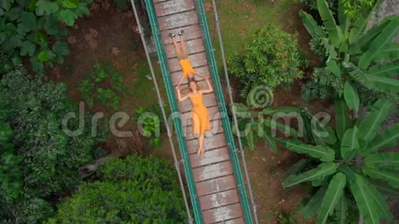 一名年轻女子和她的小儿子躺在丛林上的吊桥上的空中射击前往东南部视频的预览图