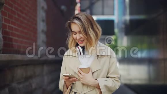 慢动作的漂亮年轻女士拿着智能手机触摸屏幕在户外喝咖啡城市生活方式视频的预览图