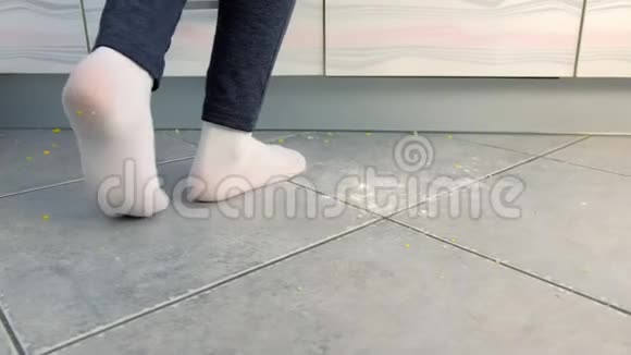 女人站在厨房肮脏的地板上做饭厨房地板上的剩菜和面包屑穿着白色袜子的腿视频的预览图