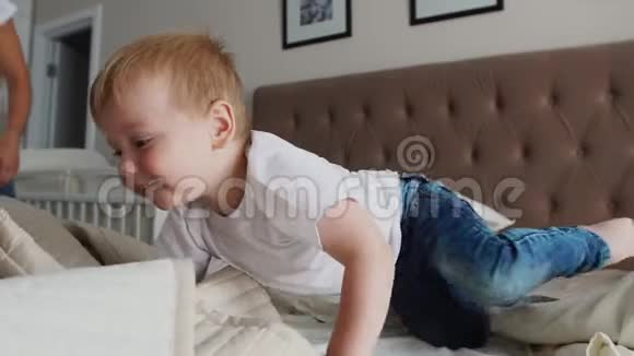 年轻的母亲和父亲带着她两岁的小儿子穿着睡衣在床上放松和玩耍视频的预览图