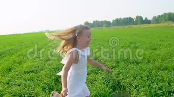 金发可爱的小女孩穿着白色连衣裙在绿色的田野上奔跑微笑着孩子孩子在花园里跑笑视频的预览图