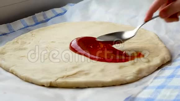 厨师用勺子在披萨面团上撒番茄酱视频的预览图
