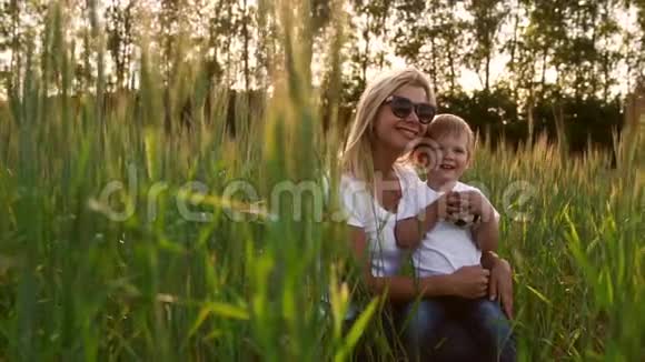 爱的母亲和儿子拥抱和玩足球在田野与小穗在美丽的夕阳光白色的t视频的预览图