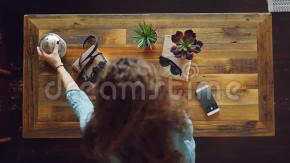 年轻女性将相机植物和太阳镜放在桌子上然后用智能手机拍照制作荧光屏视频的预览图