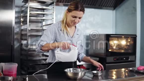 一个女人的特写一个穿着蓝色衬衫穿着黑色围裙的糖果人在金属碗里搅拌面团加入视频的预览图