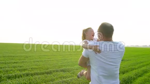 父亲和幸福的童女女儿在夕阳的绿野里爸爸和小女儿玩他拥抱她视频的预览图