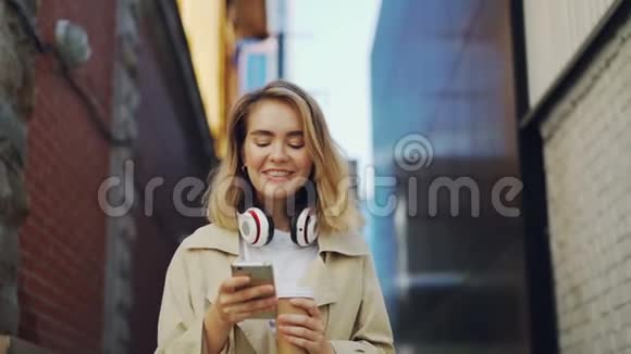 慢动作的快乐女孩使用智能手机而走在街上穿着外套拿着外卖咖啡城市视频的预览图