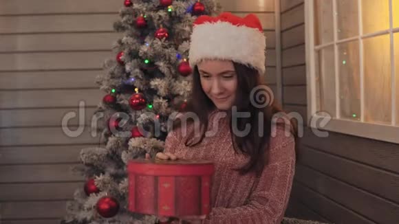 带圣诞帽的年轻女孩打开礼物女孩带着圣诞礼物微笑视频的预览图