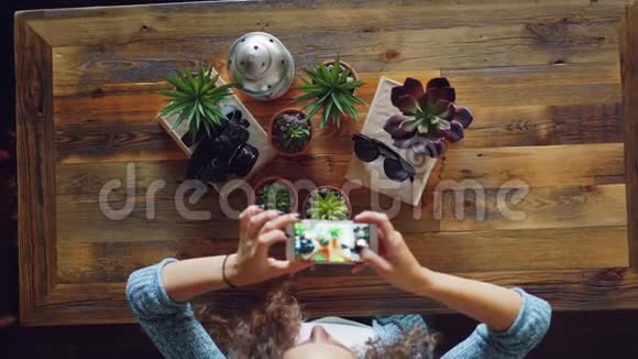 创意摄影师用智能手机在木桌上拍摄植物照相机和太阳镜的平躺照片视频的预览图