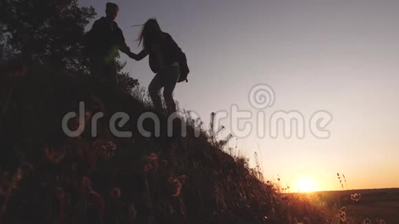 男性旅行者向攀登山顶的女性旅行者伸出手游客们在夕阳下爬山视频的预览图