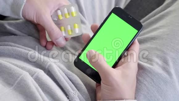男人坐在沙发上用智能手机安装绿色的模拟屏幕然后吃药视频的预览图