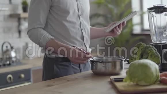 不可辨认的男人在衬衫上煮汤检查食谱在厨房里的平板电脑上概念视频的预览图