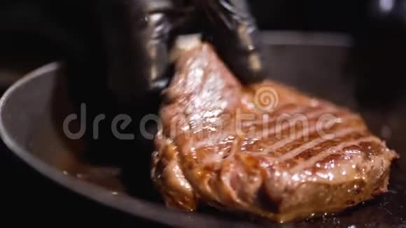 用黑色橡胶手套将美味的煎牛排举在煎锅上视频的预览图