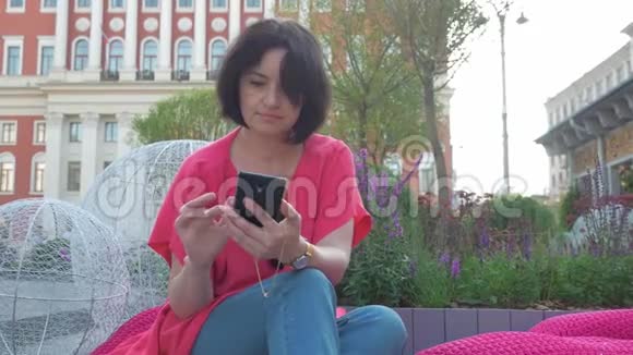 一个女人在城里用手机她坐在花丛中在一个美丽的地方放松视频的预览图