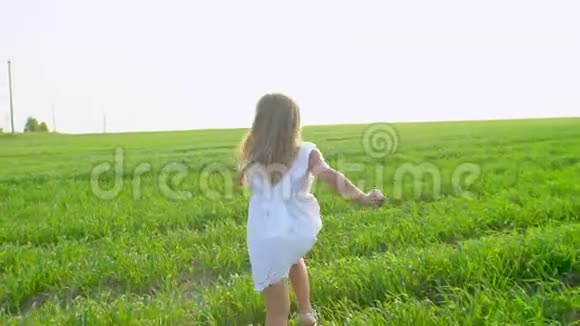 金发可爱的小女孩穿着白色连衣裙在绿色的田野上奔跑微笑着孩子孩子在花园里跑笑视频的预览图