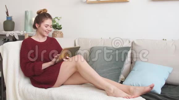 穿针织毛衣的可爱女孩在网上购物休息日看电视视频的预览图