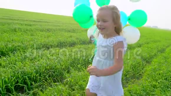 穿着裙子的小女孩手里拿着气球穿过绿色的麦田孩子孩子在花园里跑视频的预览图