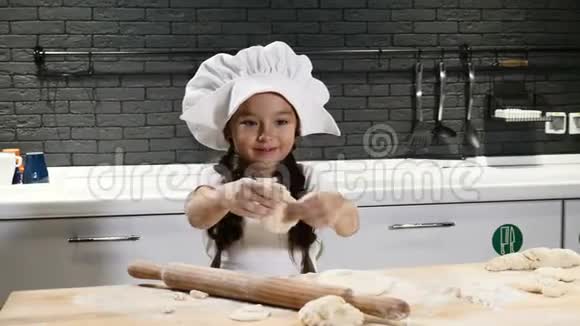 戴着厨师帽和围裙的漂亮女孩小厨师的概念可爱的女孩玩面团4k视频的预览图
