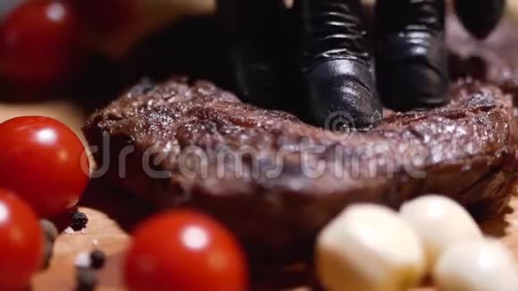 用黑色橡胶手套将一块肉压在一块切肉板上靠近多汁的红西红柿和洋葱视频的预览图