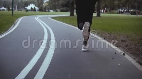 人沿着弯弯曲曲的公园路奔跑后景慢动作穿白色运动鞋的运动员在安静的小巷里慢跑视频的预览图