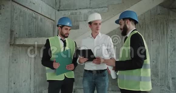 三位自信的商业建筑师戴着防护头盔站在现场用平板电脑讨论了视频的预览图