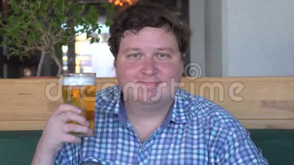 快乐的年轻白种人胖子拿着一杯啤酒在酒吧工作后对着镜头微笑视频的预览图