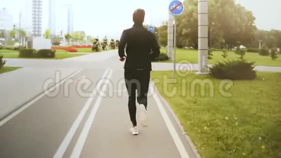4K人沿着城市公园路跑步后景穿黑色运动服的健身运动员白色运动鞋健康的生活方式视频的预览图