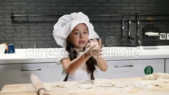 小厨师的概念穿着厨师帽和厨师围裙用面团做饭的漂亮小女孩年轻的炊具持有滚针4k视频的预览图