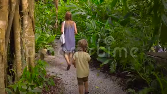 Steadycam拍摄了一位年轻妇女和她的儿子她正在参观一个热带花园里面有异国情调的果树和植物视频的预览图