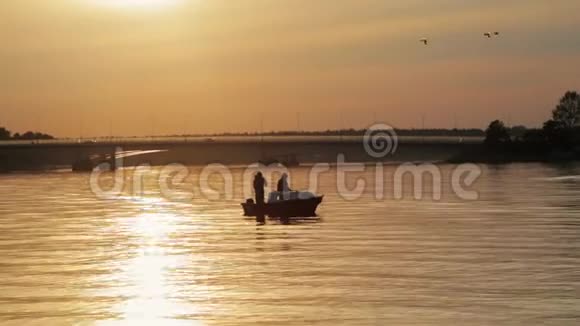 日落时分湖中一艘船上有钓竿的两名渔民的剪影视频的预览图