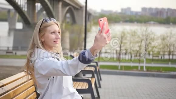 年轻漂亮的金发女郎用智能手机自拍一位年轻女子沿着河堤散步视频的预览图