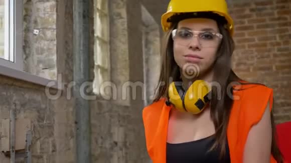 年轻迷人的女性戴着头盔耳机和眼镜看着对着镜头微笑着女建筑工人视频的预览图