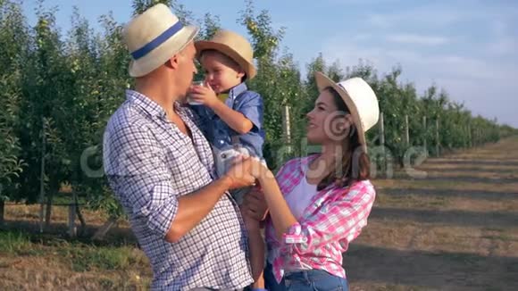 家庭在苹果园快乐的年轻父母带着孩子戴着草帽喝着干净的水视频的预览图