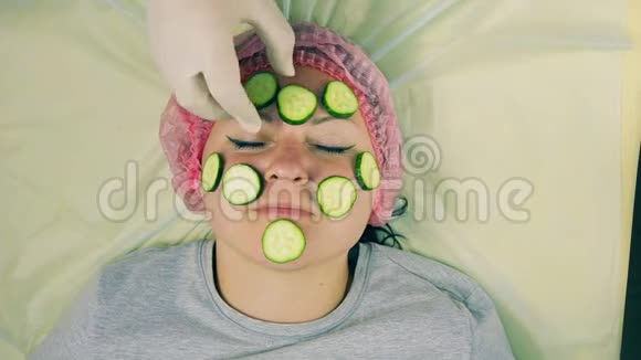 戴手套的男性美容师的手从女性脸上取出黄瓜视频的预览图