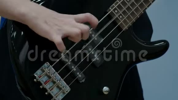 少年弹黑色电动低音吉他的手指特写他在一部音乐剧里拉了弦视频的预览图