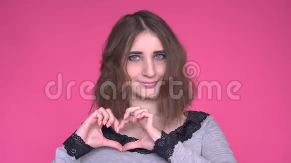 爱肖像微笑的女人做心脏标志象征用手隔离粉红色的墙壁背景视频的预览图