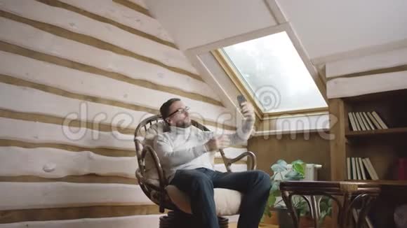 戴眼镜的成年男子坐在椅子上的智能手机摄像头上自拍照视频的预览图