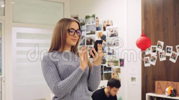 戴眼镜的年轻女人在办公室里使用智能手机短信网上冲浪APP社交网络视频的预览图