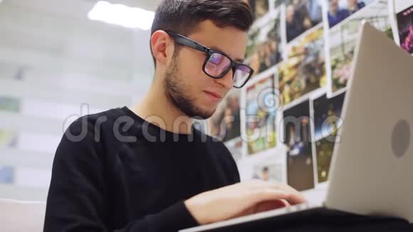 在办公室背景下年轻时尚的商人戴着眼镜在智能手机和笔记本电脑上打字视频的预览图