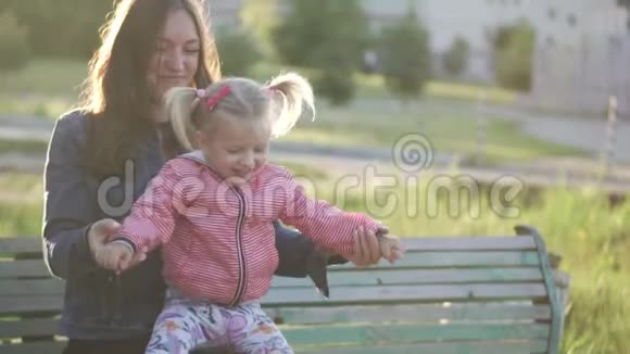 妈妈坐在长凳上她腿上有个小女孩外面一个温暖的春天视频的预览图