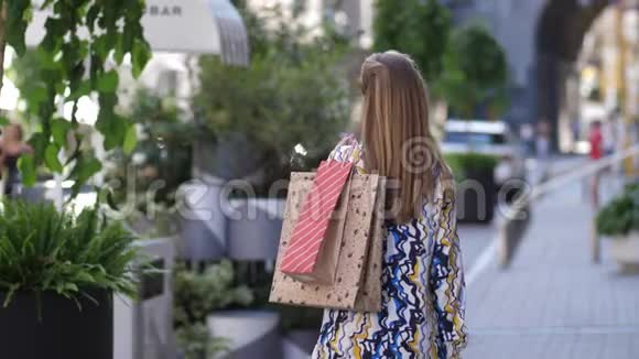 微笑的女人购物狂拿着纸袋走在街上转过身来看着摄像机的慢镜头画像视频的预览图