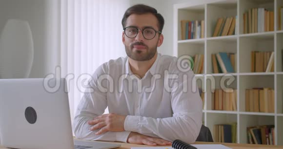 戴着笔记本电脑和看着镜头微笑的眼镜的成年英俊高加索商人的特写肖像视频的预览图