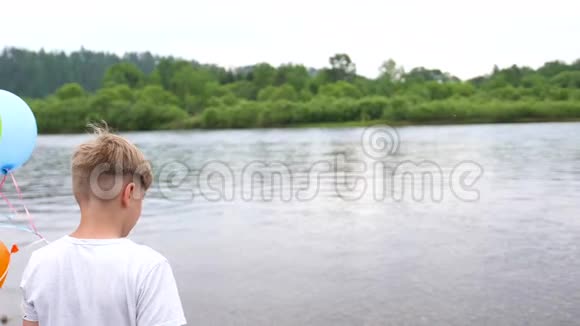 一个青少年拿着气球在湖边的大自然中度过暑假庆祝和乐趣孩子生日视频的预览图