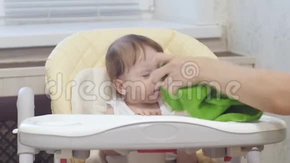 妈妈擦着婴儿的脸宝宝学会用勺子吃粥婴儿是反复无常的坐在高椅上哭泣视频的预览图