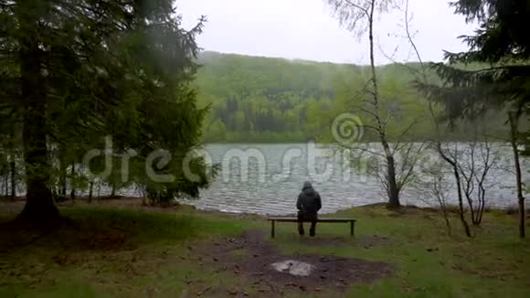 神秘孤独的人坐在湖岸的长凳上的山林雨天美丽的挪威山湖岸斯卡视频的预览图