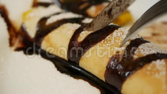 顾客用叉子和刀子吃美味的薄饼卷上面放着新鲜芒果巧克力和糖粉视频的预览图