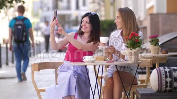 两个漂亮的年轻女人坐在咖啡馆的一张桌子上在电话4k慢动作上自拍视频的预览图